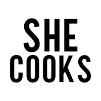 She Cooks iron-on transfer design: SHE COOKS in black on a white background