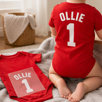 Baby Football Kit Name Number iron-on transfer: white OLLIE 1 on a red baby bodysuit, worn and as a transfer beside it