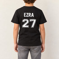 Baby Football Kit Name Number Iron-On Transfer, shown on a black kids t-shirt (back view)
