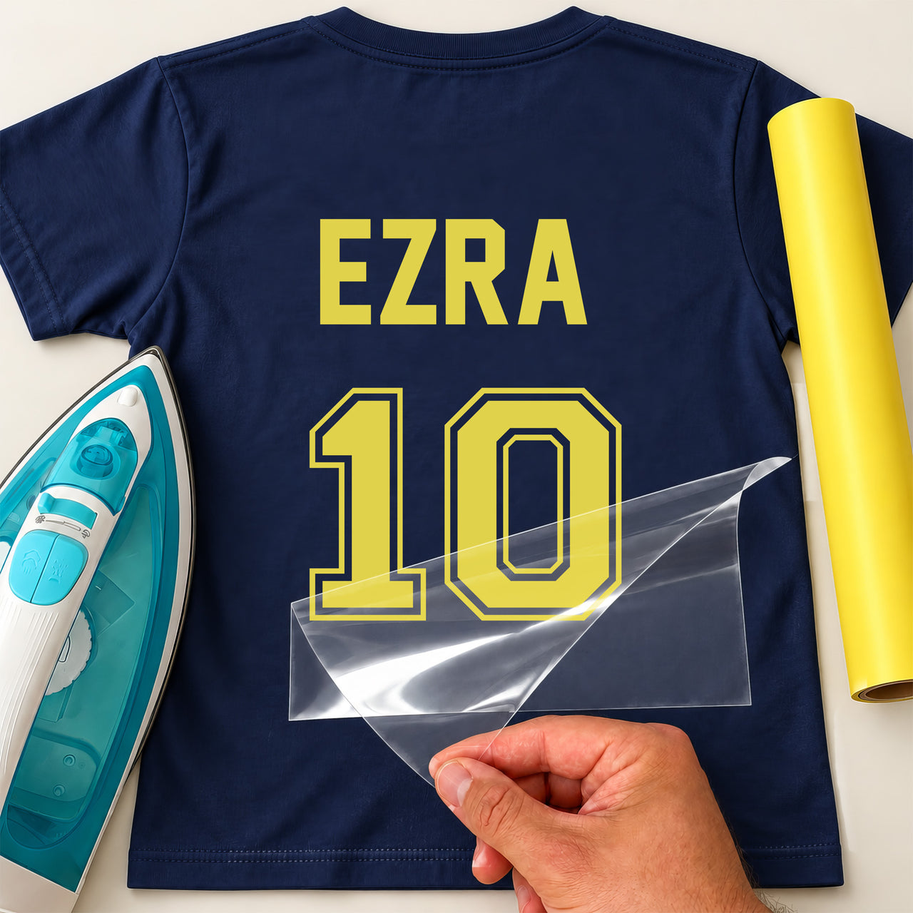 Baby Football Kit Name Number iron-on transfer: yellow EZRA 10 on a navy T-shirt, film being peeled