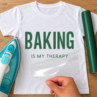 White T-shirt with green 'BAKING IS MY THERAPY' lettering, carrier film being peeled off - iron-on vinyl transfer