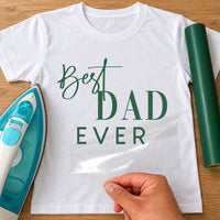 White T-shirt with green script and serif dad lettering, film peeled back beside a teal iron