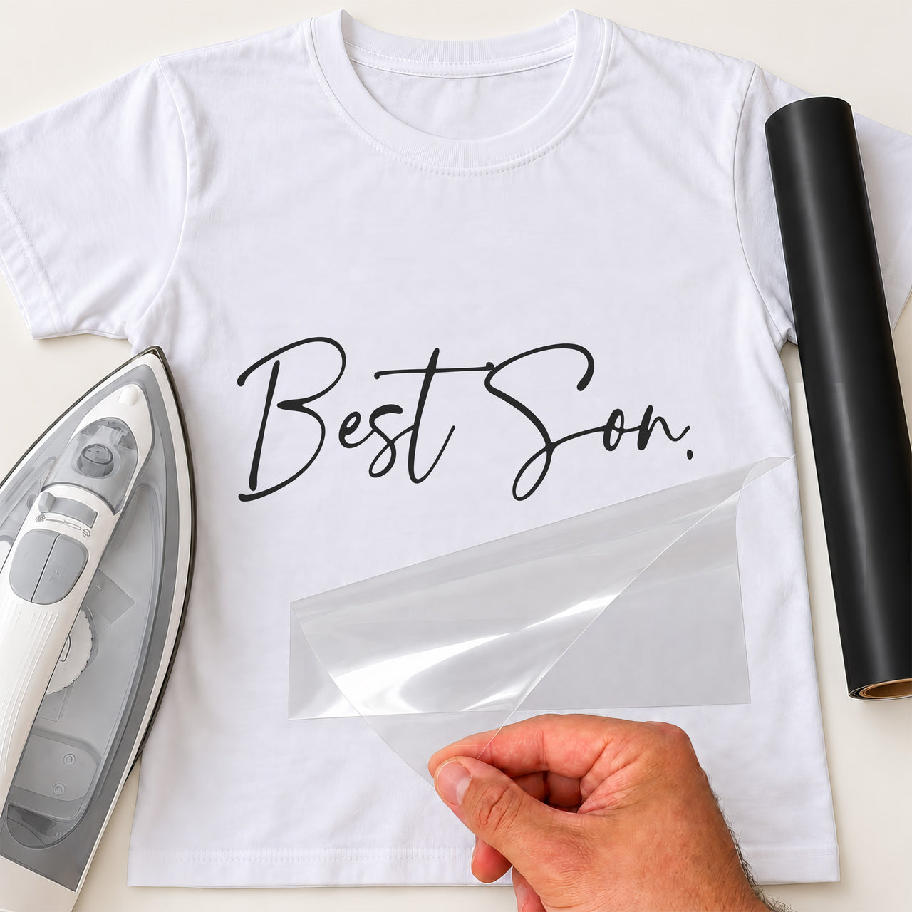 White T-shirt with black 'Best Son.' iron-on transfer in handwritten script, iron and black vinyl roll