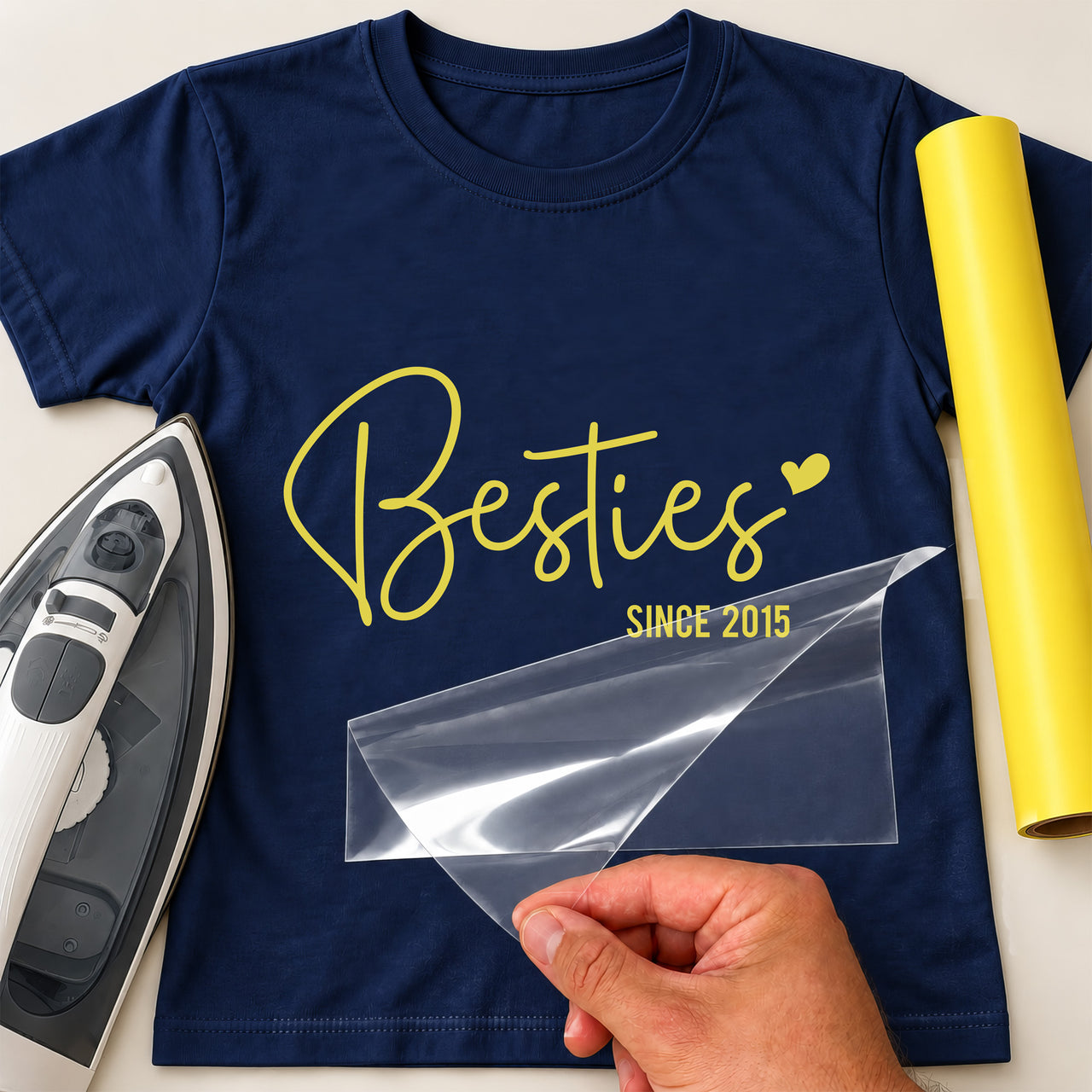 Besties iron-on transfer: yellow script Besties SINCE 2015 on a navy T-shirt, film being peeled