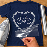 Back of a navy T-shirt with silver bicycle inside a bike chain heart, carrier film being peeled off - iron-on vinyl transfer