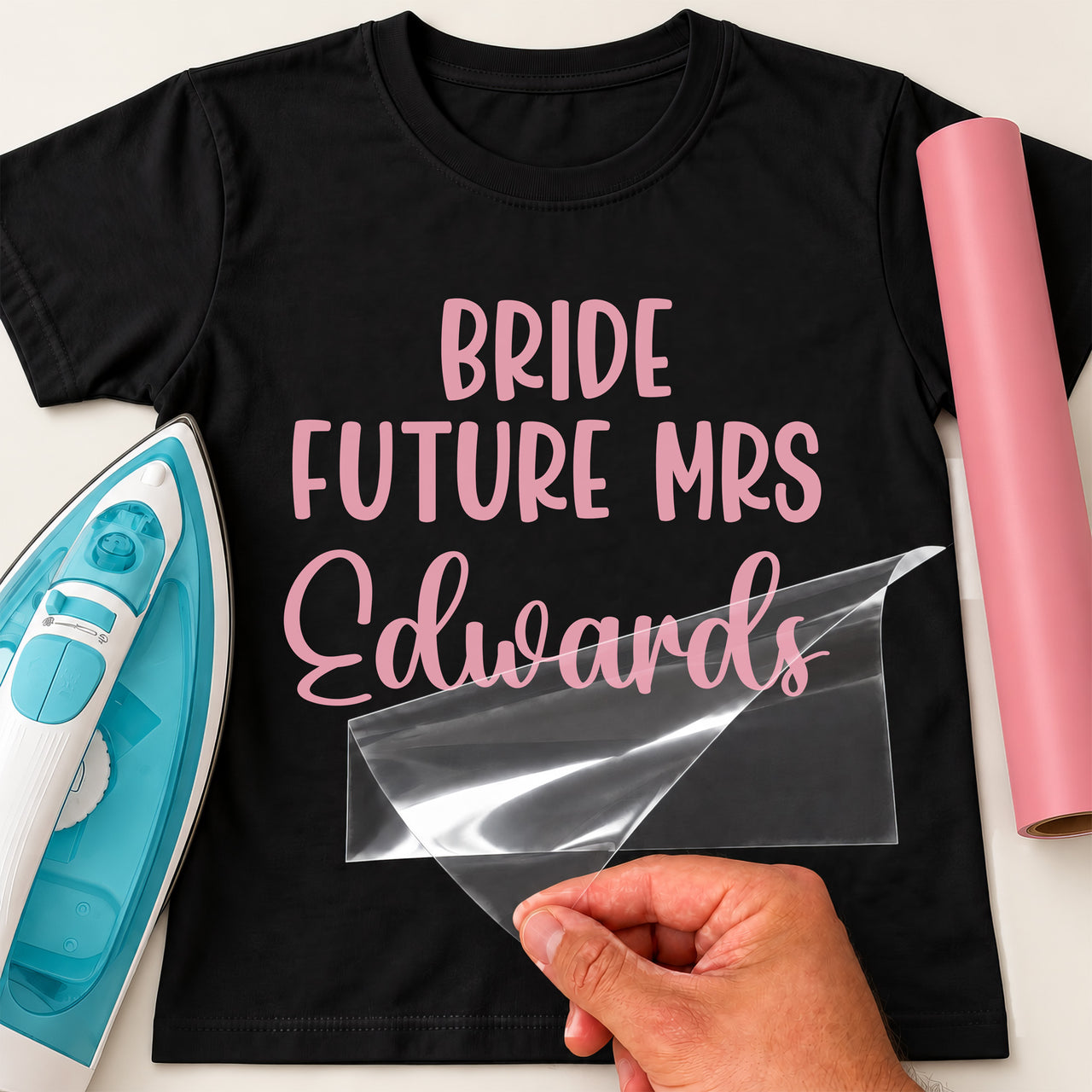 Mockup: black tee with pink "BRIDE FUTURE MRS" capitals and a script surname "Edwards", pink vinyl roll at the side