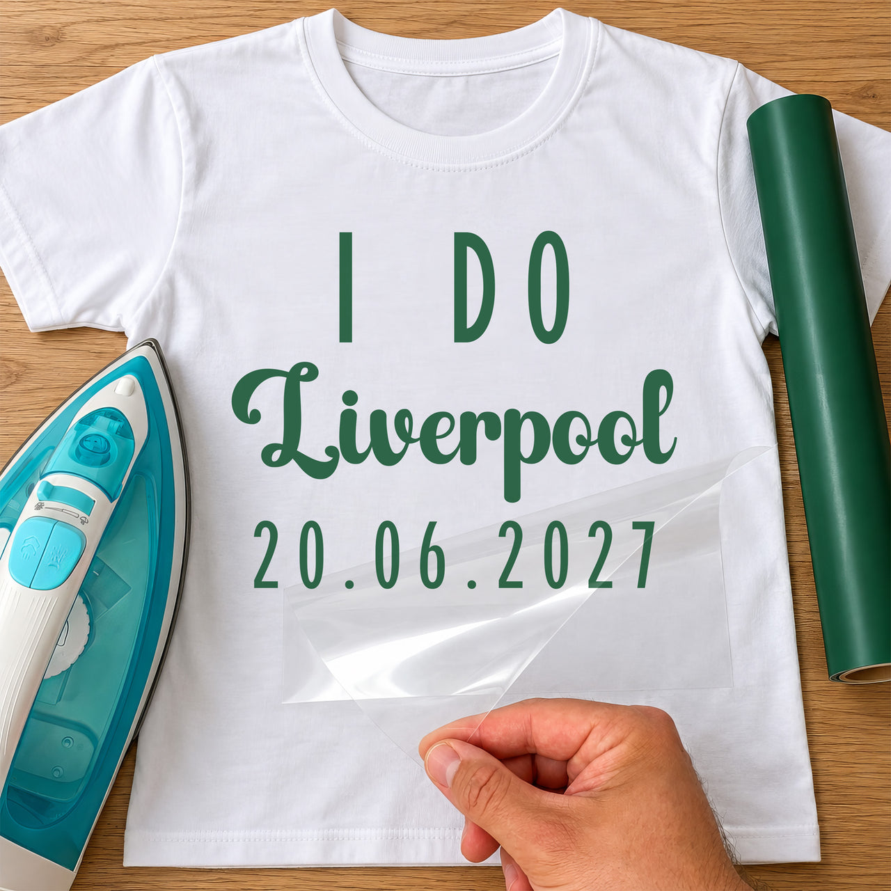 White T-shirt with green 'I DO', 'Liverpool' and '20.06.2027' lettering, personalised hen party HTV transfer being peeled