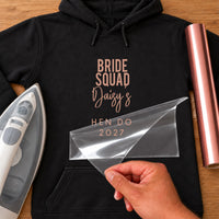 Black hoodie with rose gold iron-on vinyl reading 'BRIDE SQUAD Daisy's HEN DO 2027', iron and rose gold vinyl roll