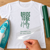 White T-shirt with green 'BRIDE TO BE' bold capitals, 'Holly' script and 'MARBELLA 20.06.2027', iron and green vinyl roll