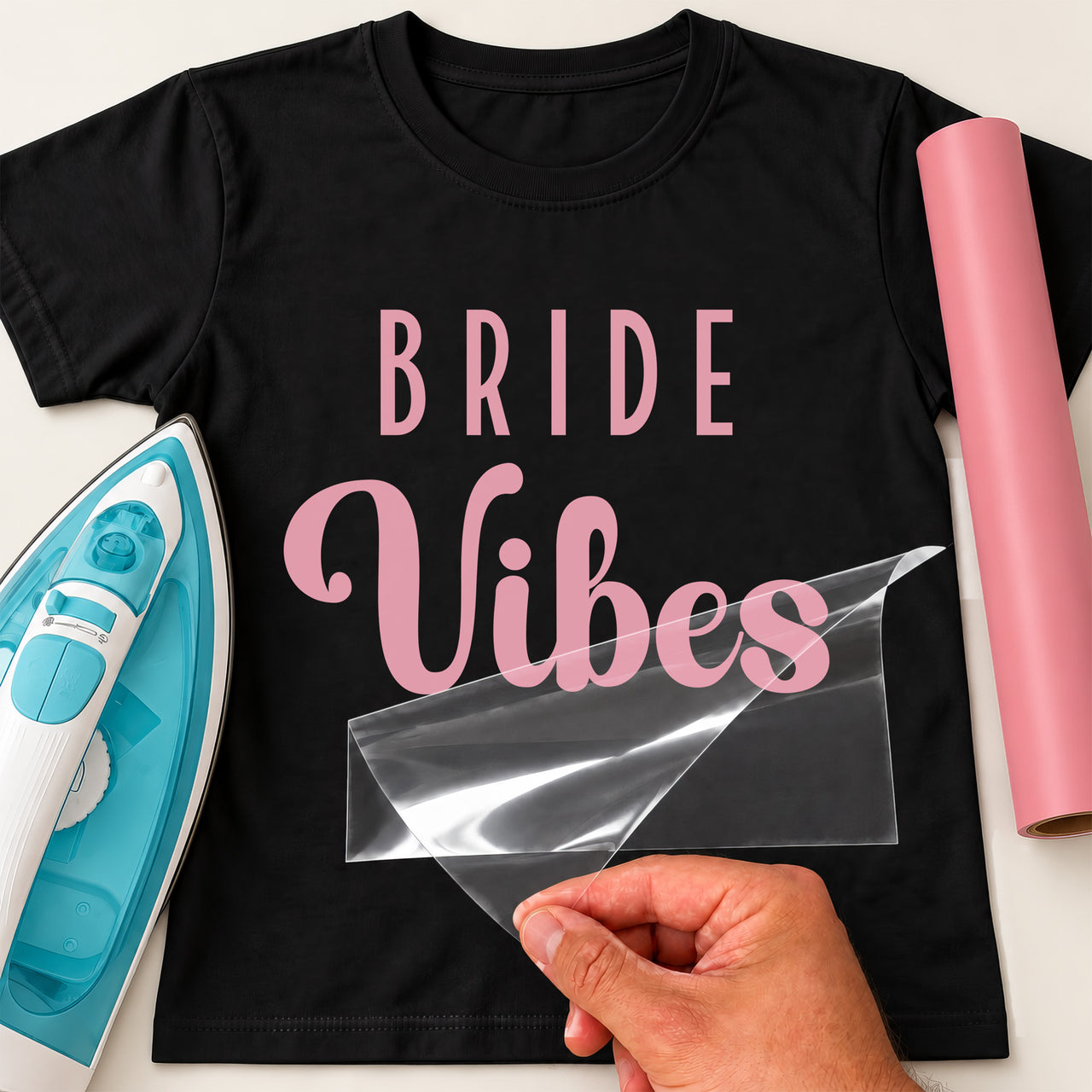 Black T-shirt with pink 'BRIDE Vibes' lettering, carrier film being peeled off - iron-on vinyl transfer