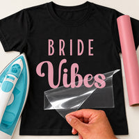 Black T-shirt with pink 'BRIDE Vibes' lettering, carrier film being peeled off - iron-on vinyl transfer