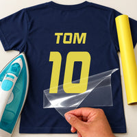 Charity Match Name Number iron-on transfer: yellow TOM 10 on a navy T-shirt, film being peeled