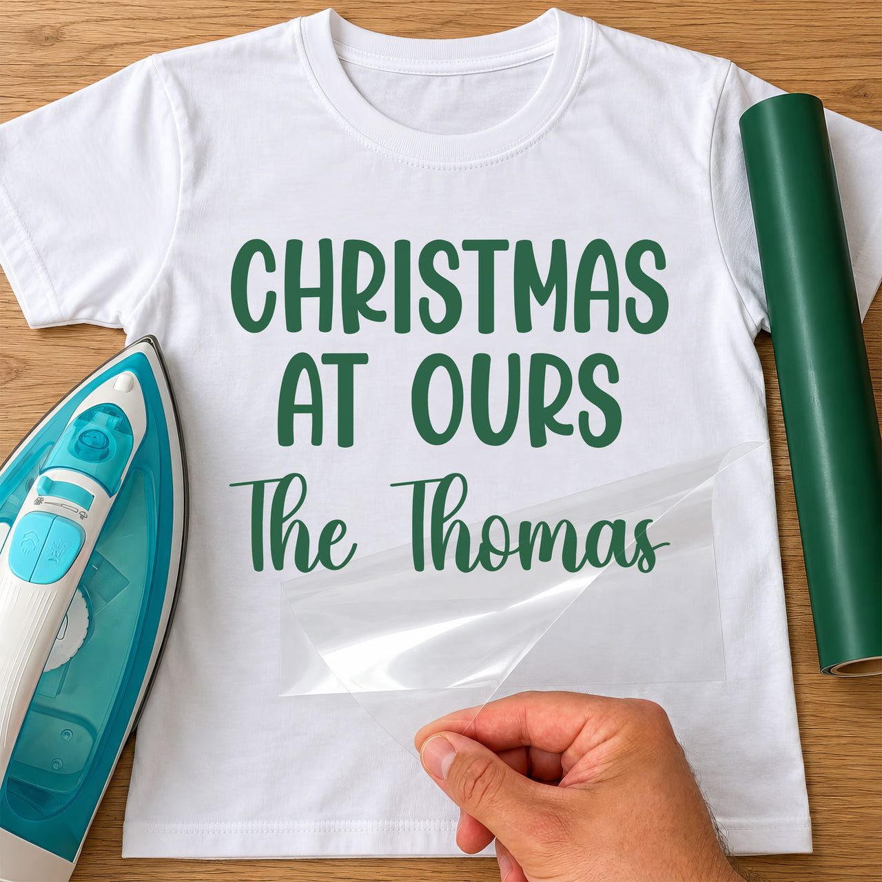 Christmas At Ours iron-on transfer: green CHRISTMAS AT OURS The Thomas on a white T-shirt, film being peeled