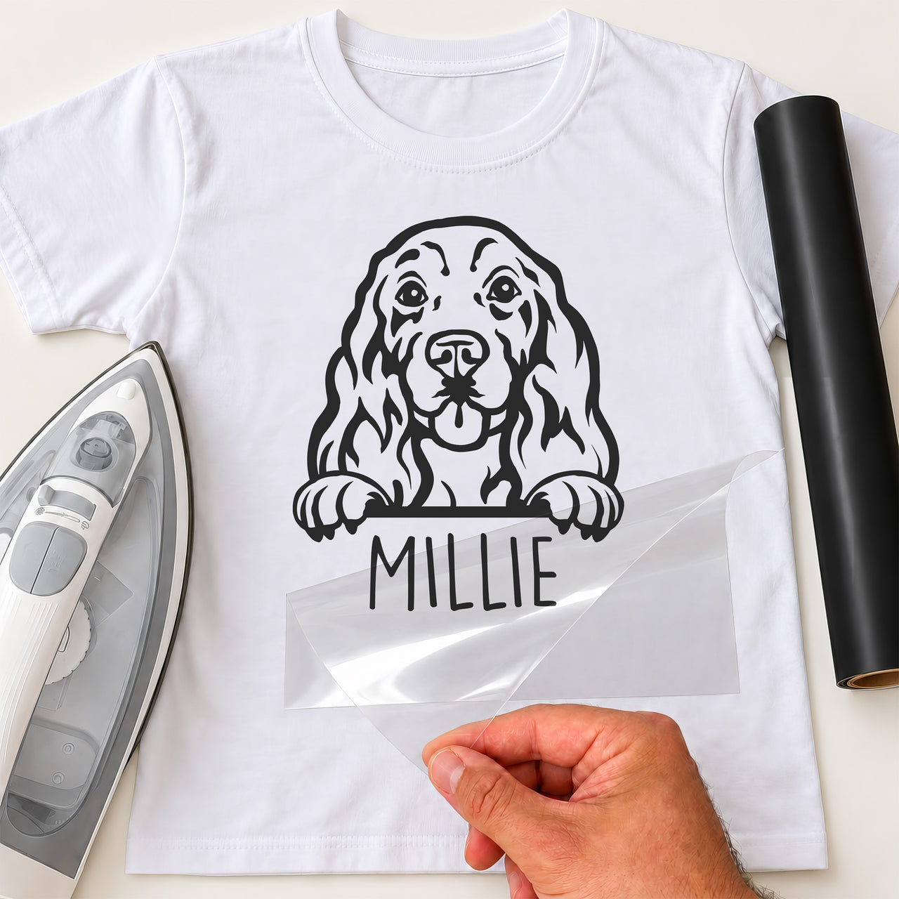 White T-shirt with black Cocker Spaniel peeking over a line and name 'MILLIE' iron-on transfer, iron and black vinyl roll