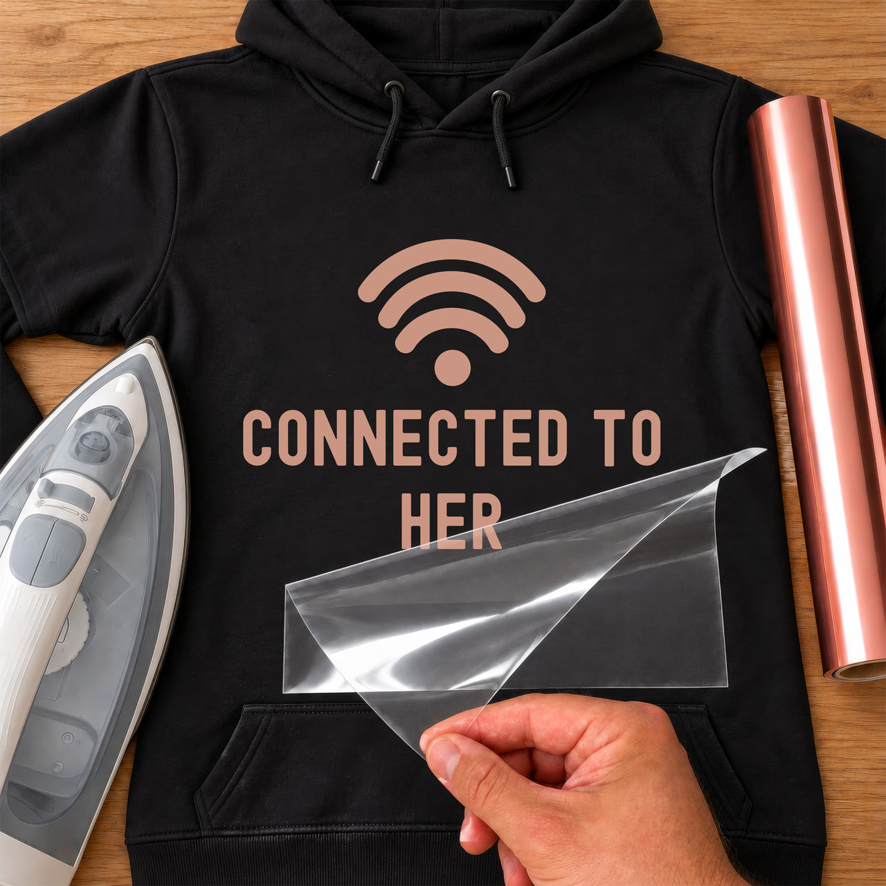 Black hoodie with rose gold wifi symbol and 'CONNECTED TO HER', carrier film being peeled off - iron-on vinyl transfer