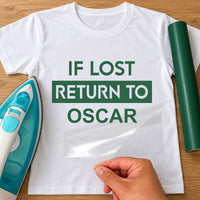 White T-shirt with green 'IF LOST RETURN TO OSCAR' lettering, carrier film being peeled off - iron-on vinyl transfer