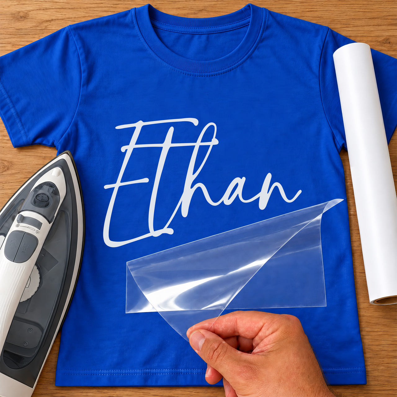 Custom Staff Name iron-on transfer: white script Ethan on a royal blue T-shirt, film being peeled