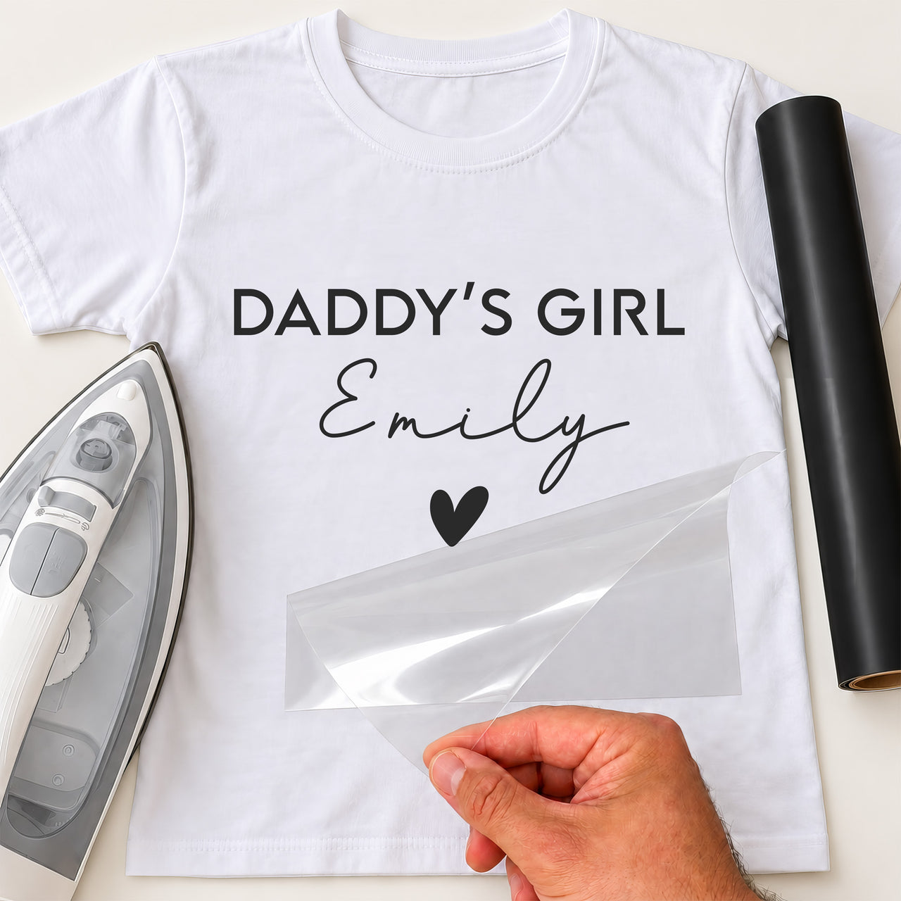 White T-shirt with black 'DADDY'S GIRL' capitals, 'Emily' script and a heart iron-on transfer, iron and black vinyl roll