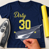 Navy T-shirt with yellow 'Dirty' script, '30' and two stars in iron-on vinyl, carrier film peeled back, iron beside
