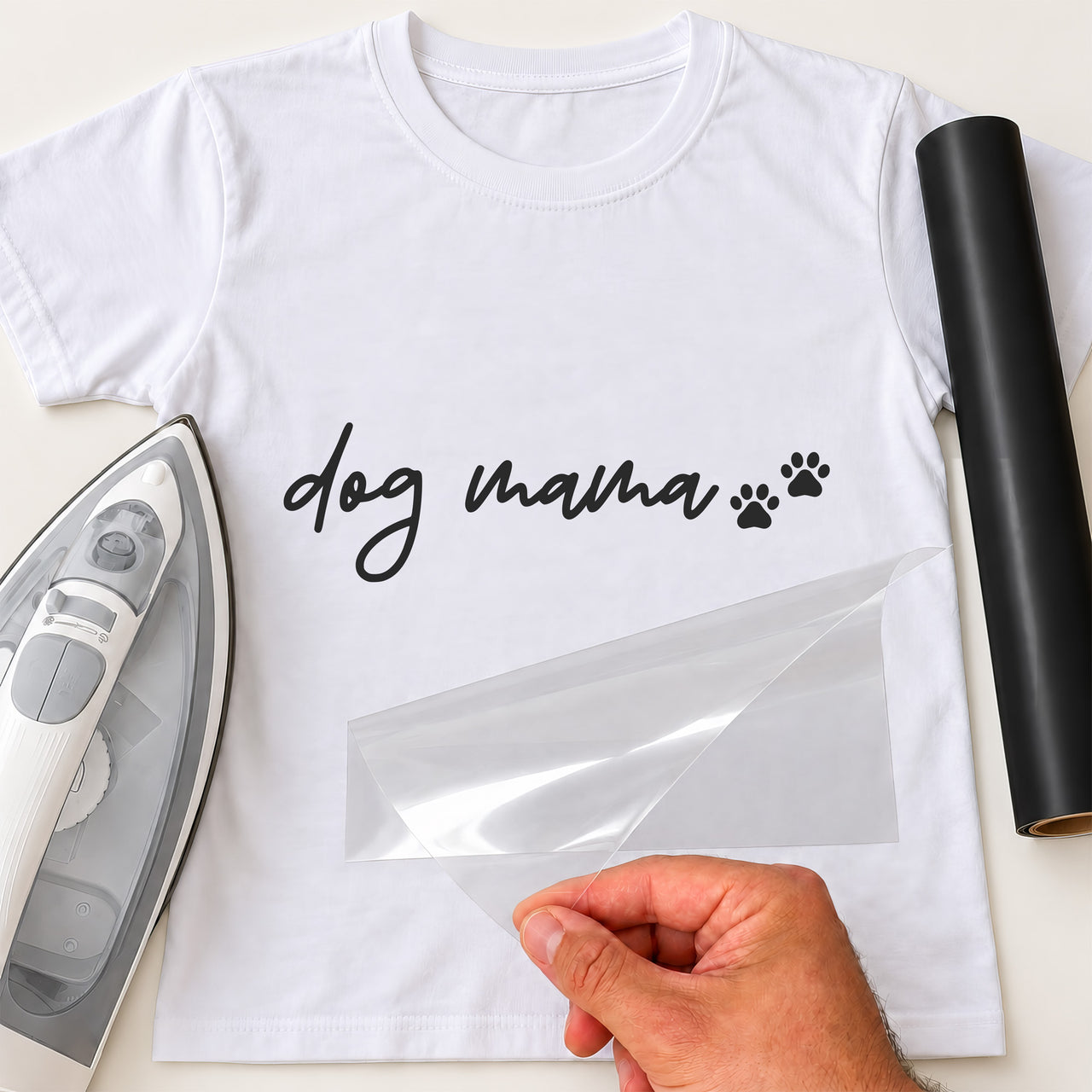 White T-shirt with black script 'dog mama' and two paw prints, carrier film being peeled off - iron-on vinyl transfer