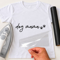 White T-shirt with black script 'dog mama' and two paw prints, carrier film being peeled off - iron-on vinyl transfer