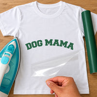 White T-shirt with green arched 'DOG MAMA' varsity lettering, carrier film being peeled off - iron-on vinyl transfer