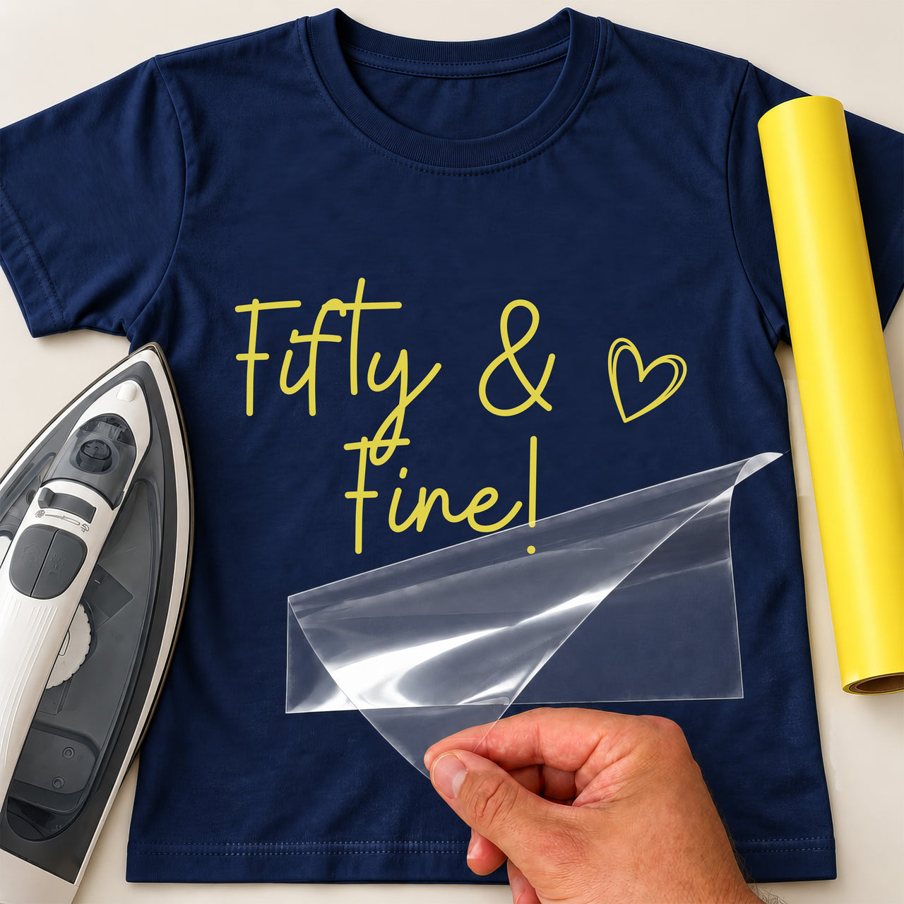 Navy T-shirt with yellow script 'Fifty & Fine!' and a heart outline, 50th birthday iron-on transfer beside a yellow roll