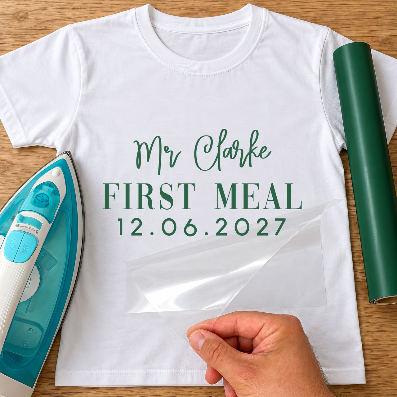 First Meal As Mr iron-on transfer: green Mr Clarke FIRST MEAL 12.06.2027 on a white T-shirt, film being peeled