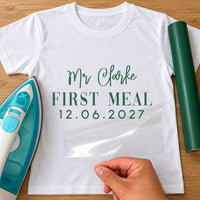 First Meal As Mr iron-on transfer: green Mr Clarke FIRST MEAL 12.06.2027 on a white T-shirt, film being peeled