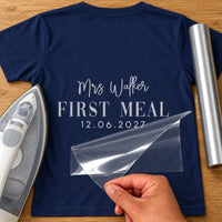 First Meal As Mrs iron-on transfer: silver Mrs Walker FIRST MEAL 12.06.2027 on a navy T-shirt, film being peeled