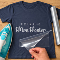 First Meal As Mrs iron-on transfer: silver FIRST MEAL AS Mrs Foster on a navy T-shirt, film being peeled