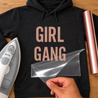 Black hoodie with rose gold 'GIRL GANG' in stacked capitals, iron-on HTV transfer being peeled from its film