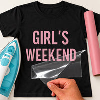 Black T-shirt with pink 'GIRL'S WEEKEND' block letters as heat transfer vinyl, film being lifted by hand
