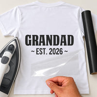 White T-shirt with black 'GRANDAD' and '~ EST. 2026 ~' iron-on transfer, iron and black vinyl roll