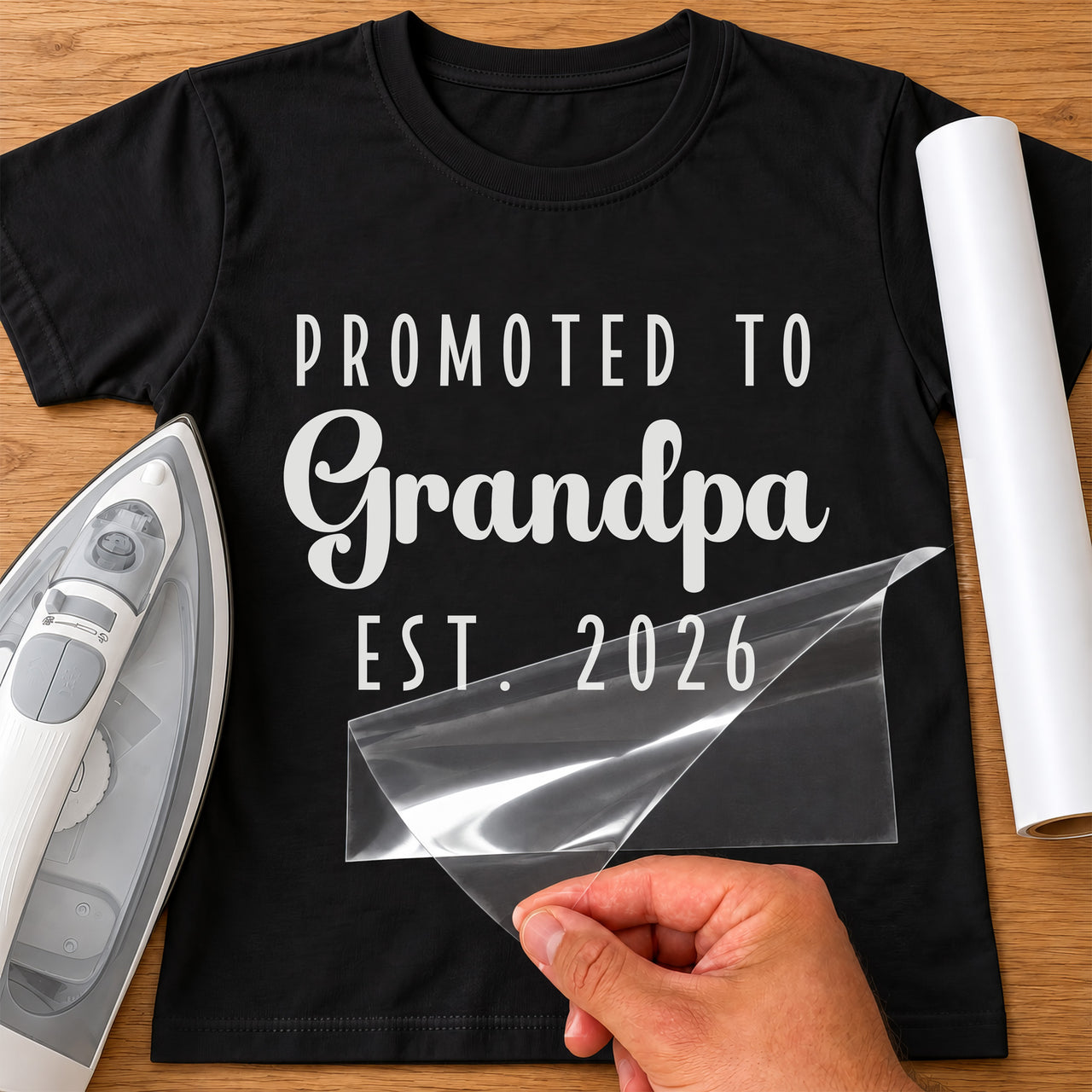 Mockup: black tee with white "PROMOTED TO Grandpa EST. 2026", script on the middle line, iron and white vinyl roll