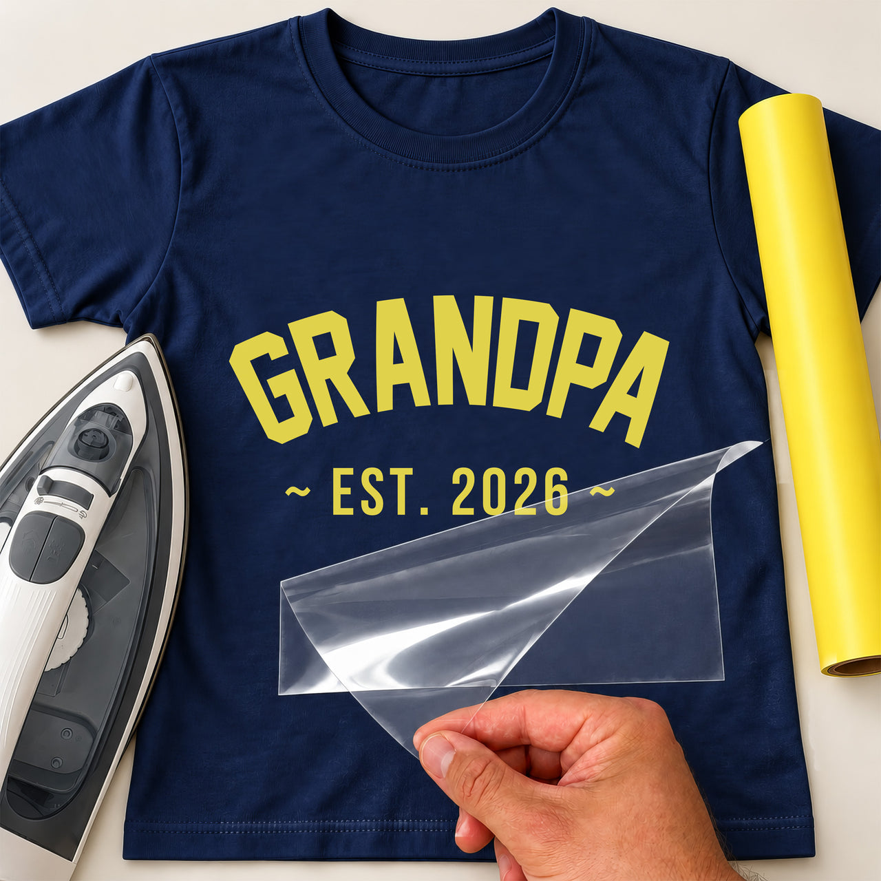 Navy T-shirt with yellow arched 'GRANDPA' and 'EST. 2026' iron-on transfer, iron and yellow vinyl roll