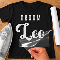 Black T-shirt with white 'GROOM' and 'Leo' name iron-on transfer, capitals over bold script, iron and white vinyl roll