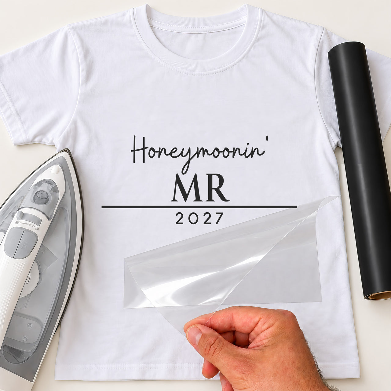 White T-shirt with black iron-on vinyl 'Honeymoonin' MR 2027', iron and vinyl roll beside