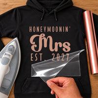 Black hoodie with rose gold 'HONEYMOONIN'' 'Mrs' 'EST. 2027' lettering, film peeled off - iron-on vinyl transfer