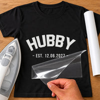 Hubby Est iron-on transfer: white HUBBY EST. 12.06.2027 on a black T-shirt, film being peeled