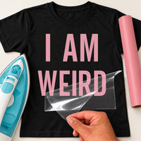 I Am Weird iron-on transfer: pink I AM WEIRD on a black T-shirt, film being peeled