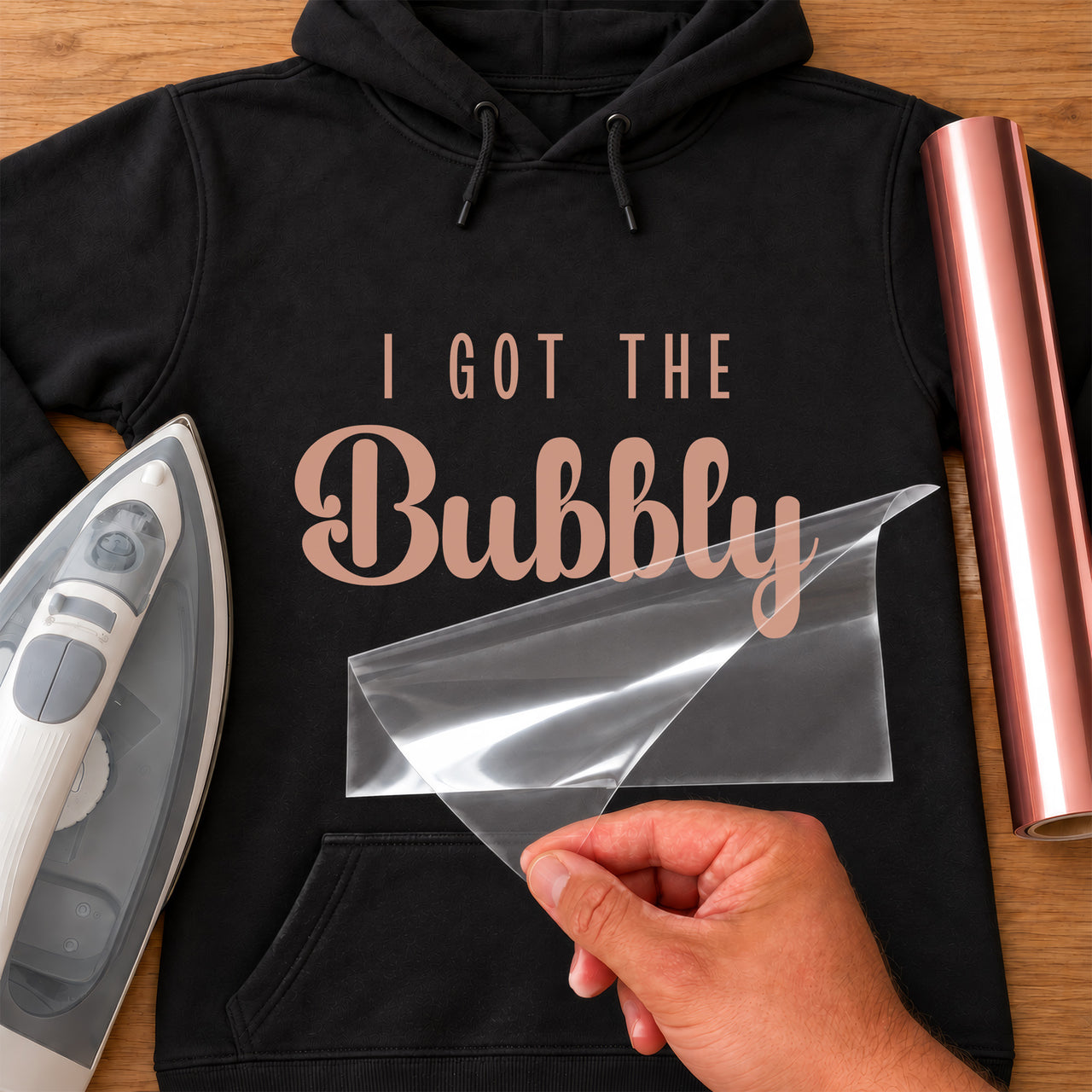 Black hoodie with rose gold iron-on vinyl 'I GOT THE Bubbly' slogan, iron and vinyl roll beside
