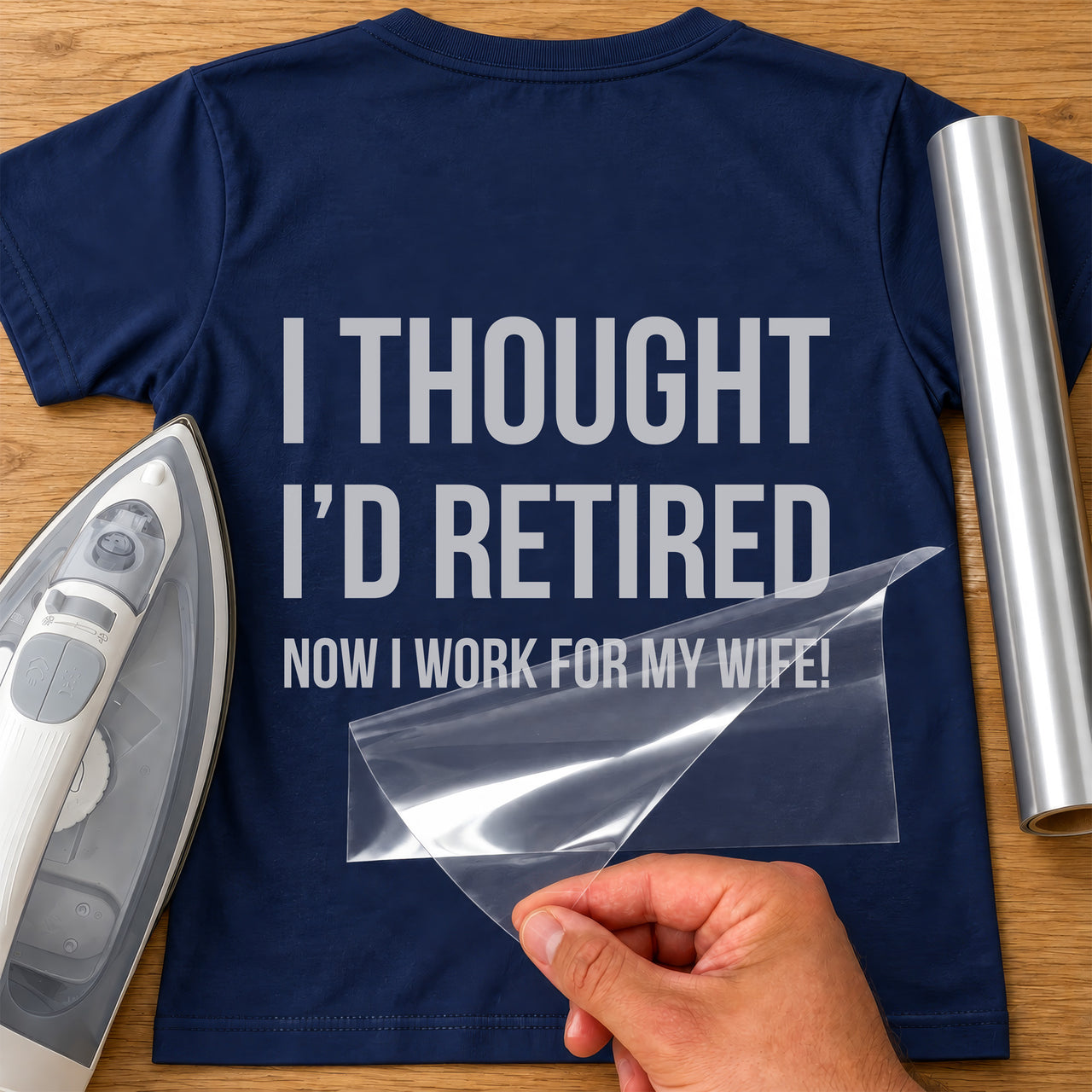 Mockup: back of a navy tee with grey vinyl 'I thought I'd retired, now I work for my wife!', carrier peeling