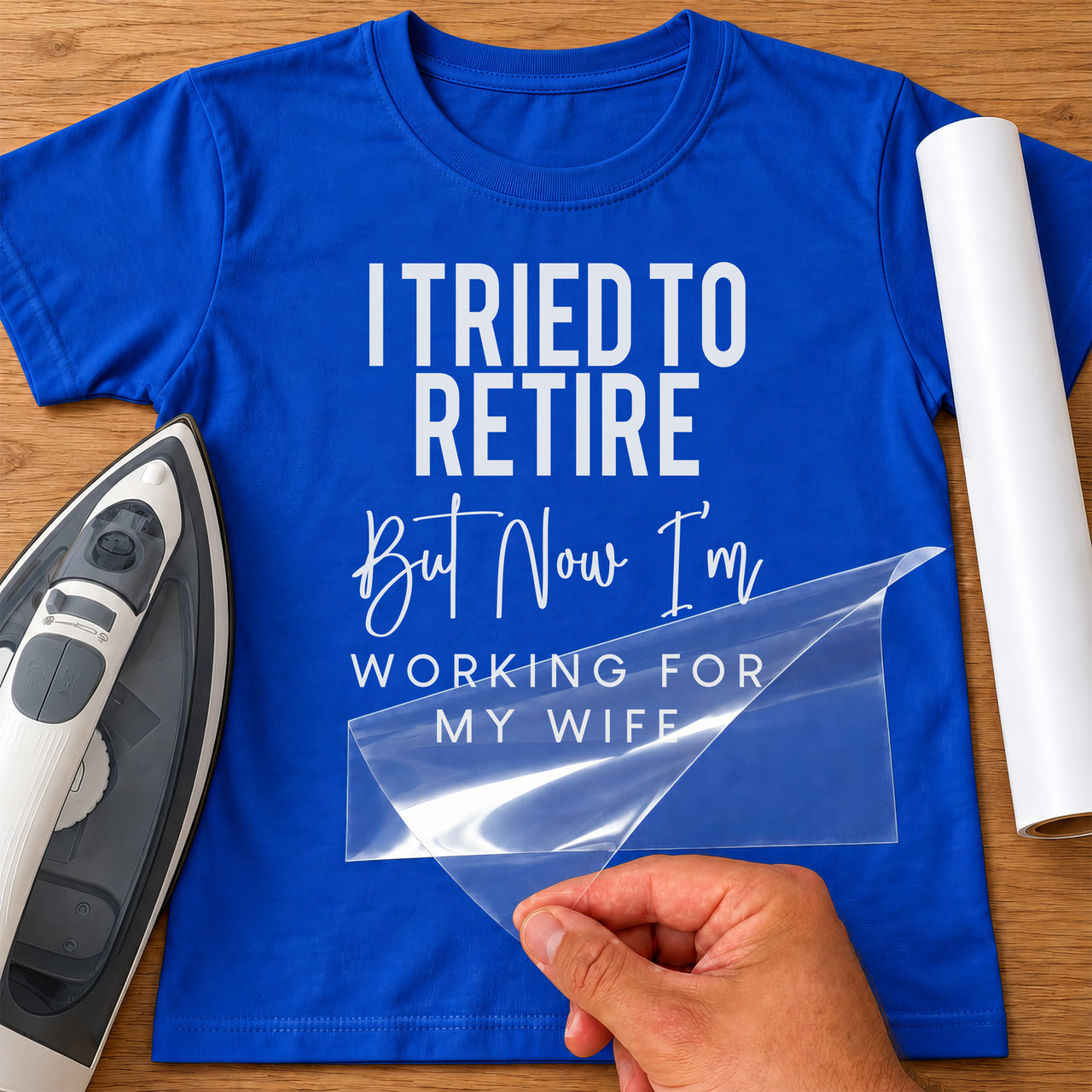Blue T-shirt with white retirement slogan transfer, carrier film being peeled off next to an iron