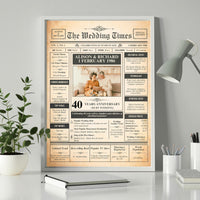 Silver framed 40th anniversary newspaper style poster on a desk beside a plant, lamp and notebook