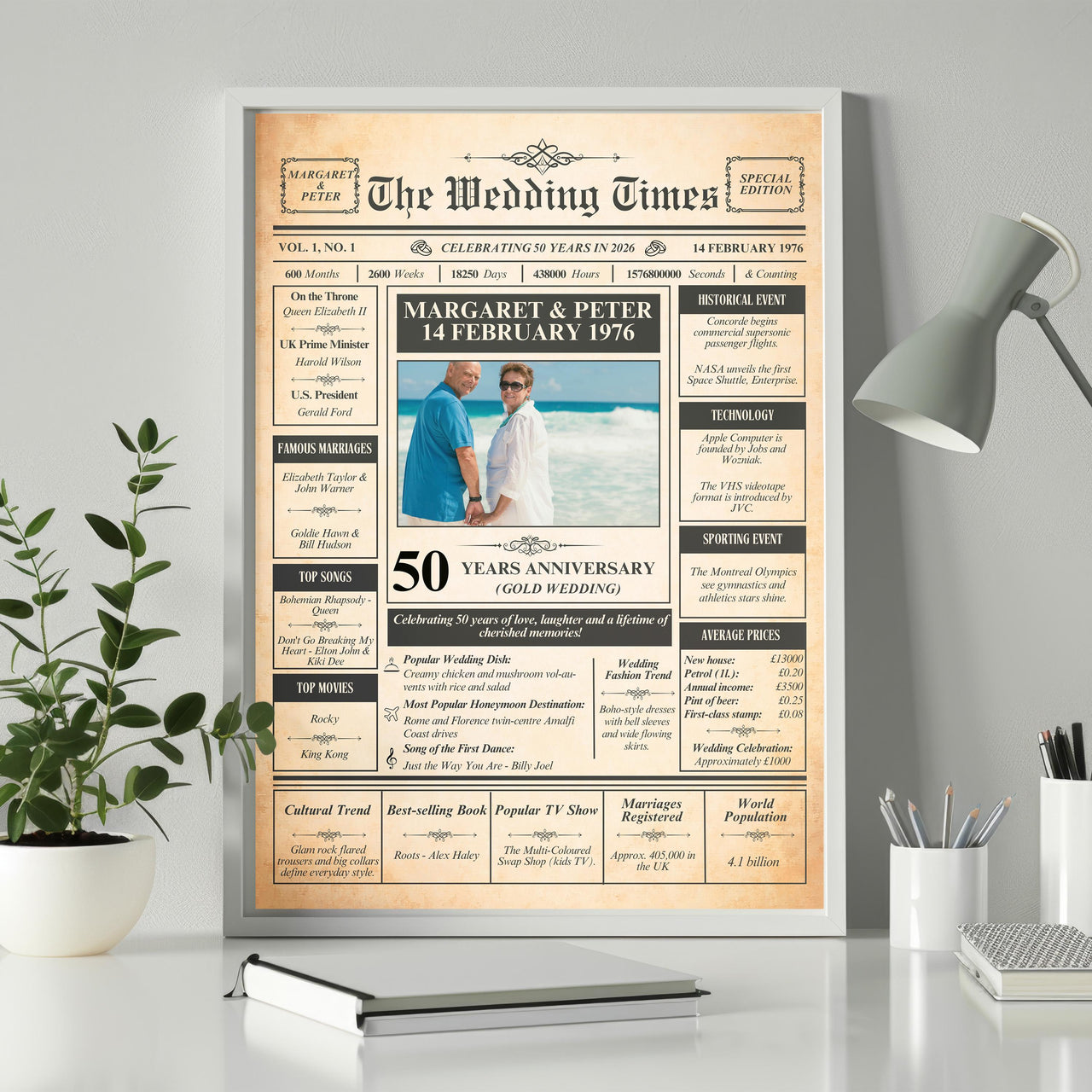 Gold wedding anniversary newspaper poster in a white frame on a desk beside a plant, lamp and notebook
