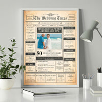 Gold wedding anniversary newspaper poster in a white frame on a desk beside a plant, lamp and notebook