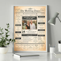 Silver wedding newspaper style print in a grey frame on a white desk beside a lamp, plant and notebook