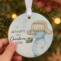 First Christmas bauble: pale blue ornament with a snowman in a fur hat holding a gift and ARTHUR'S First Christmas 2026