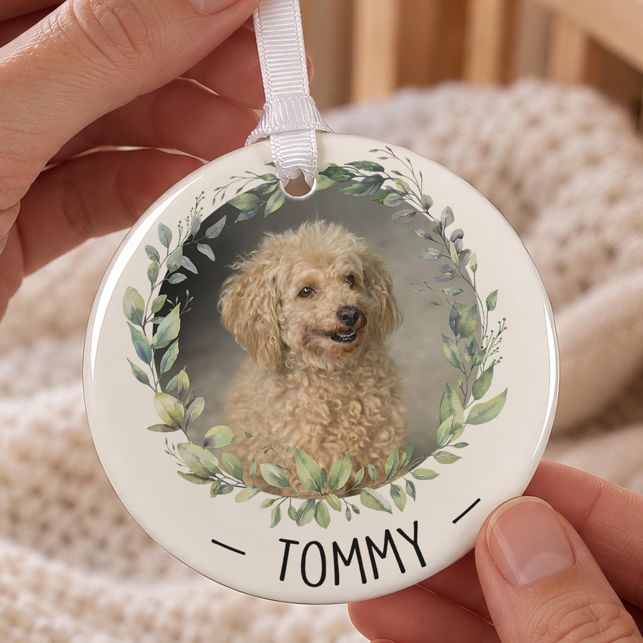 Personalised pet bauble: ceramic ornament with a dog photo inside a green leaf wreath and the name TOMMY below
